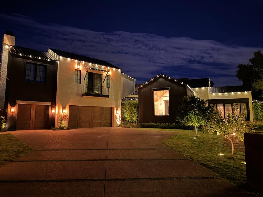 A modern farmhouse with warm lights along its metal roofline